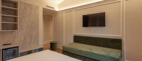 A bedroom with a bed, a green bench, a TV mounted on the wall, and built-in shelving.