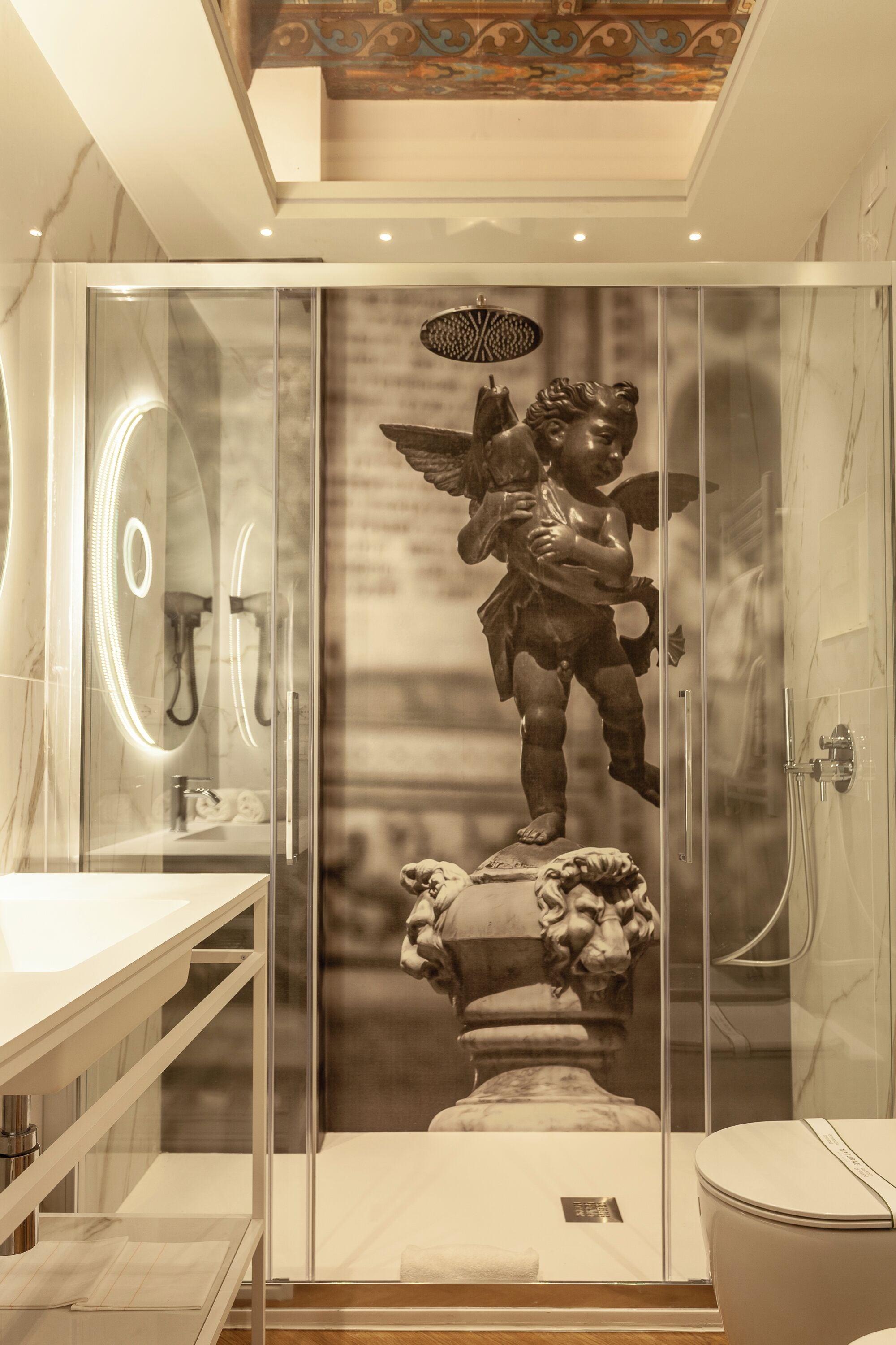 Une salle de bain moderne avec une douche à parois de verre, un meuble-lavabo en marbre et une statue d’ange décorative.