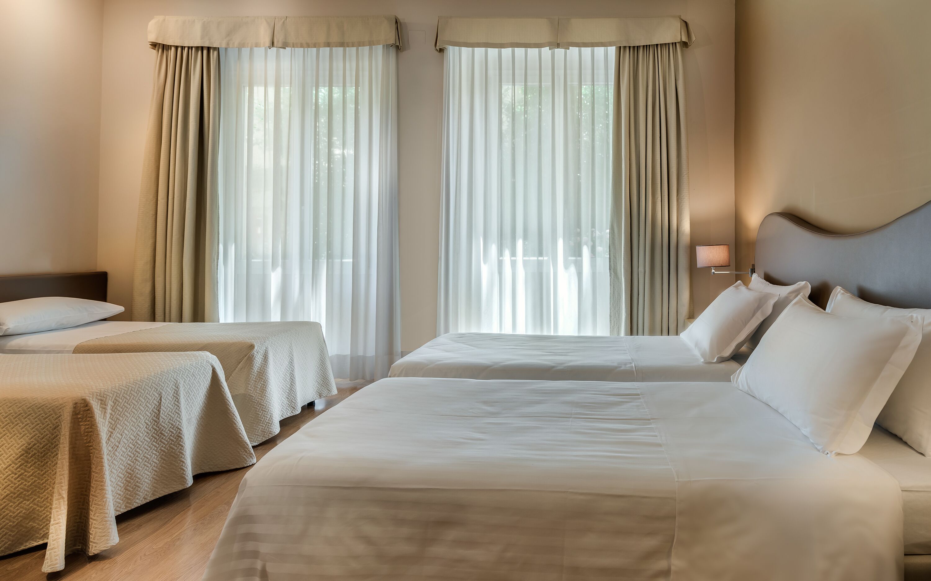 Una habitación de hotel con dos camas, cada una con cabecero, y una mesita de noche con lámpara.