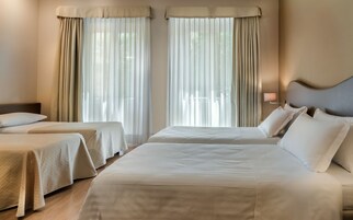 Una camera d'albergo con due letti, ognuno con testiera e comodino con lampada.
