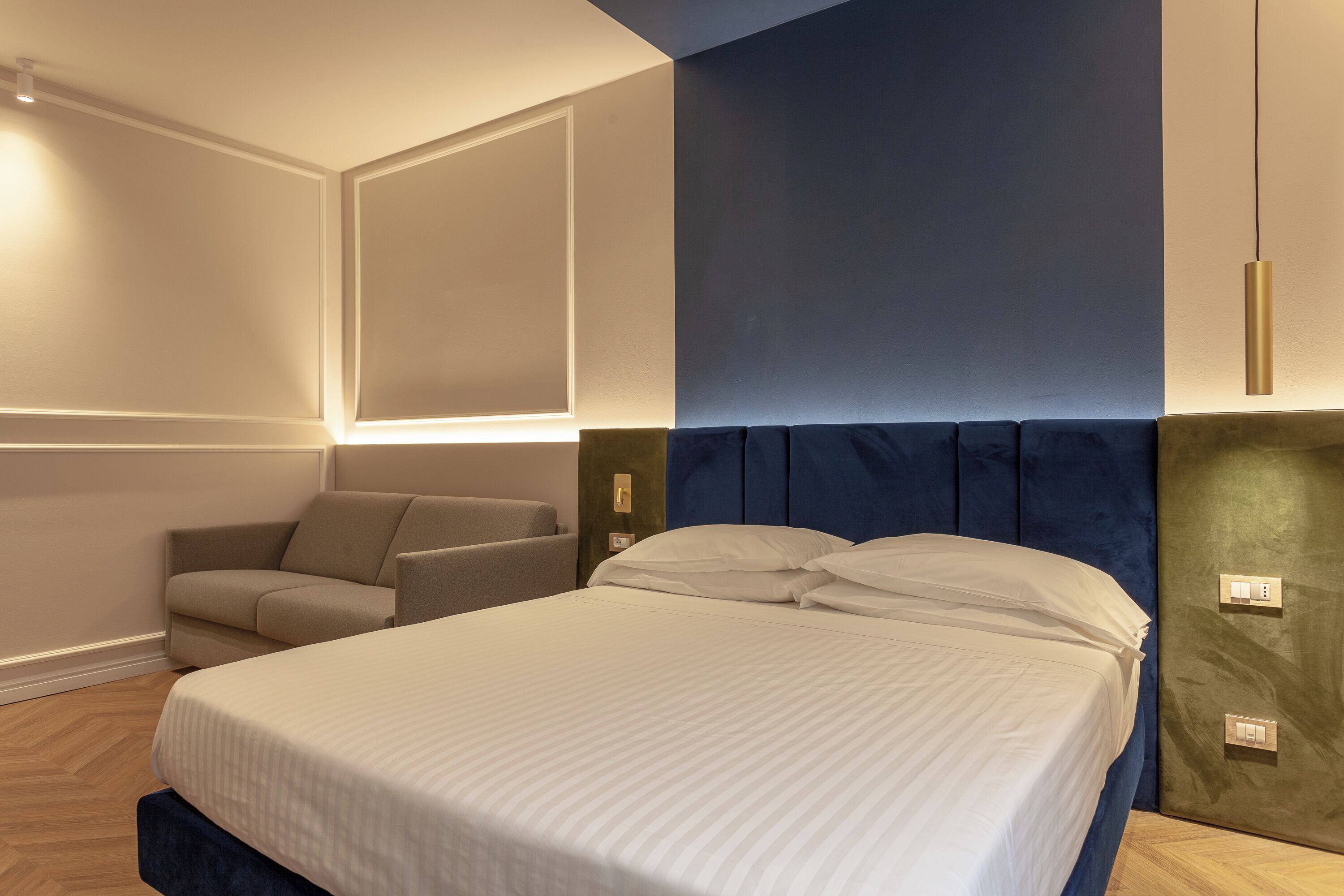 Una habitación de hotel moderna con una cama grande, un área de descanso con sofá e iluminación en la pared.
