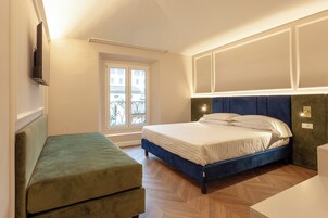 Una camera da letto con un letto, una panca verde, una finestra e una TV montata a parete.