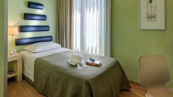 Habitación de hotel con cama, mesita de noche, lámpara, silla y ventana con cortinas.