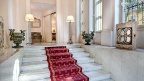 Una gran escalera con alfombra roja que lleva a una habitación con un amplio ventanal y una pared de piedra decorativa.