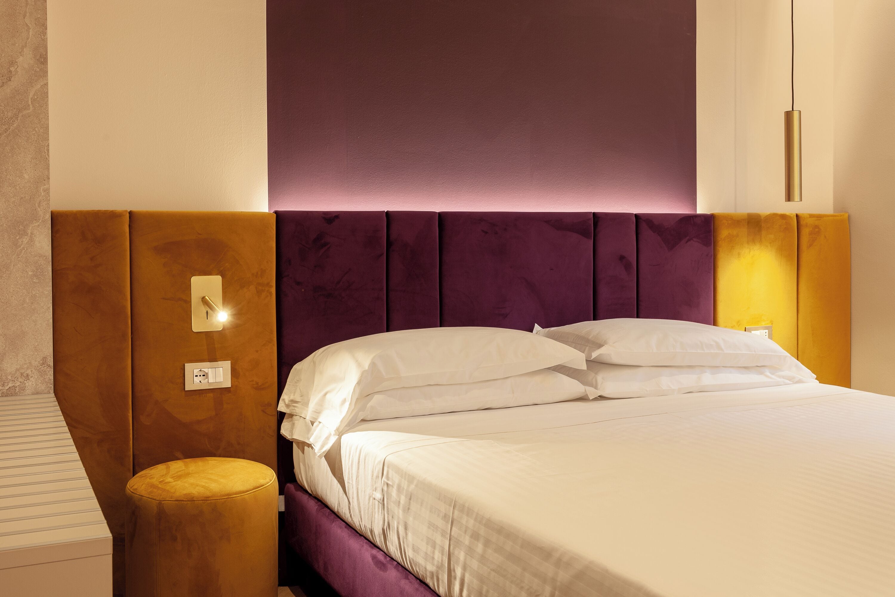 A neatly made bed with white linens and a purple headboard.