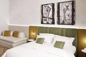 Une chambre d’hôtel avec un lit, deux canapés et des œuvres d’art accrochées au mur.