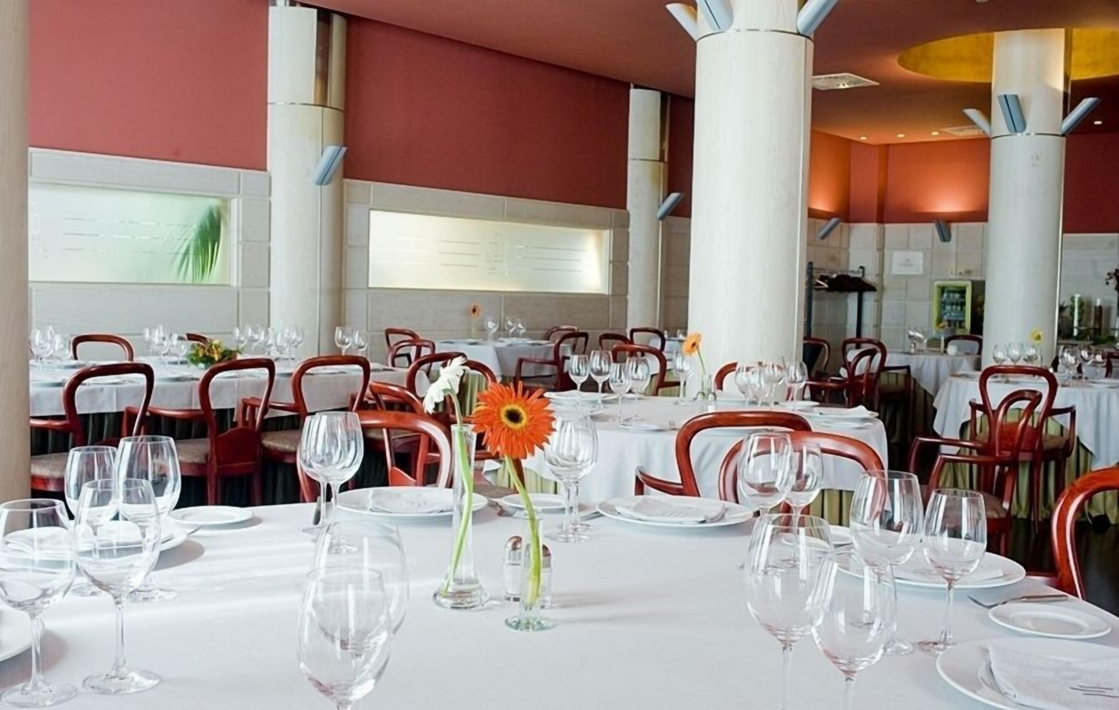 Un restaurante con varias mesas dispuestas para comer, con manteles blancos y sillas rojas.