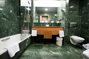 Un baño con piso de mármol, tocador de madera, cabina de ducha de vidrio, tina blanca y un inodoro.