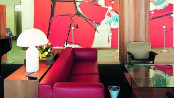 En moderne lobby med en rød sofa, et glasbord og et stort abstrakt maleri på væggen.