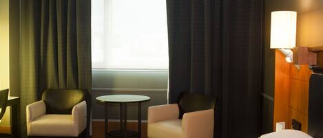Una habitación de hotel con una cama, dos sillones, una mesita y una ventana con cortinas.