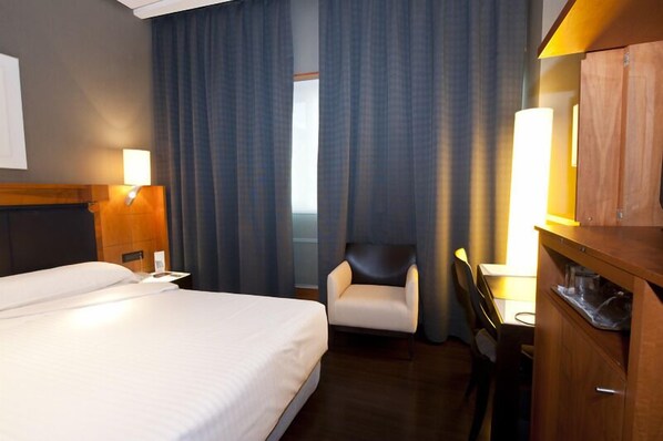Una habitación de hotel con una cama, un escritorio, una silla y un armario.