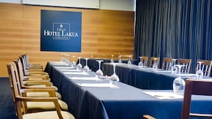 Una sala de conferencias en el Gran Hotel Lakuá, con una larga mesa dispuesta para reuniones, sillas de madera y una pantalla grande que muestra el nombre del hotel.