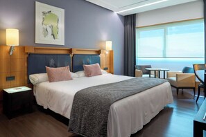 Habitación de hotel con una cama grande, dos mesitas de noche, un escritorio con una silla y vistas al exterior.