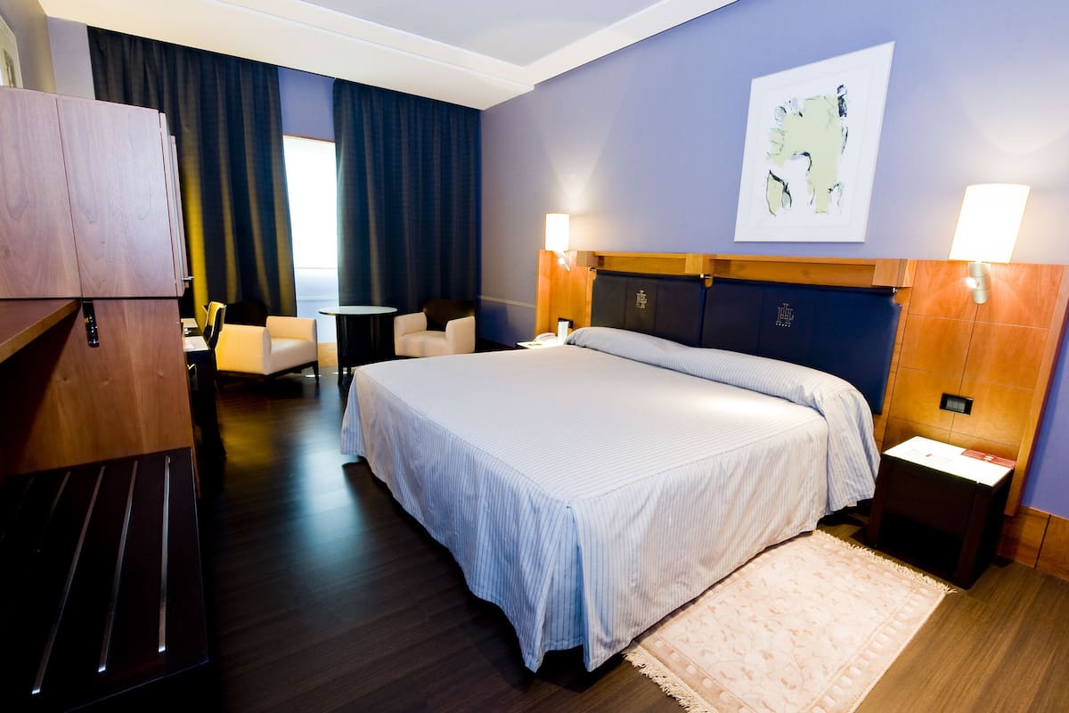 A hotel room with a large bed, a desk, a chair, and a wardrobe.