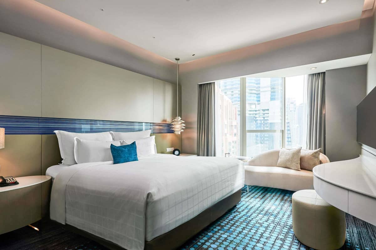 A hotel room with a large bed, a sofa, a small table, a TV, and a view of the city.