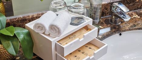 A bathroom with a marble sink, a white towel holder with towels, and a bottle of hand soap.