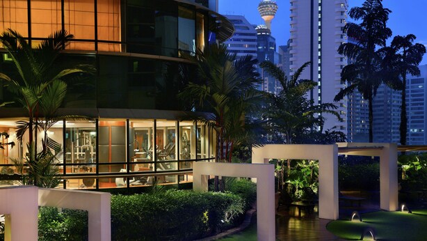 A modern hotel with a glass facade, a well-maintained garden, and a view of a tall tower in the background. - Pullman Kuala Lumpur City Centre Hotel & Residences (Kuala Lumpur)