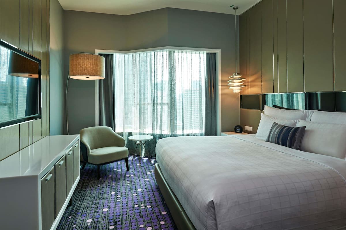 A modern hotel room with a large bed, a desk, a chair, a small table, and a window with curtains.