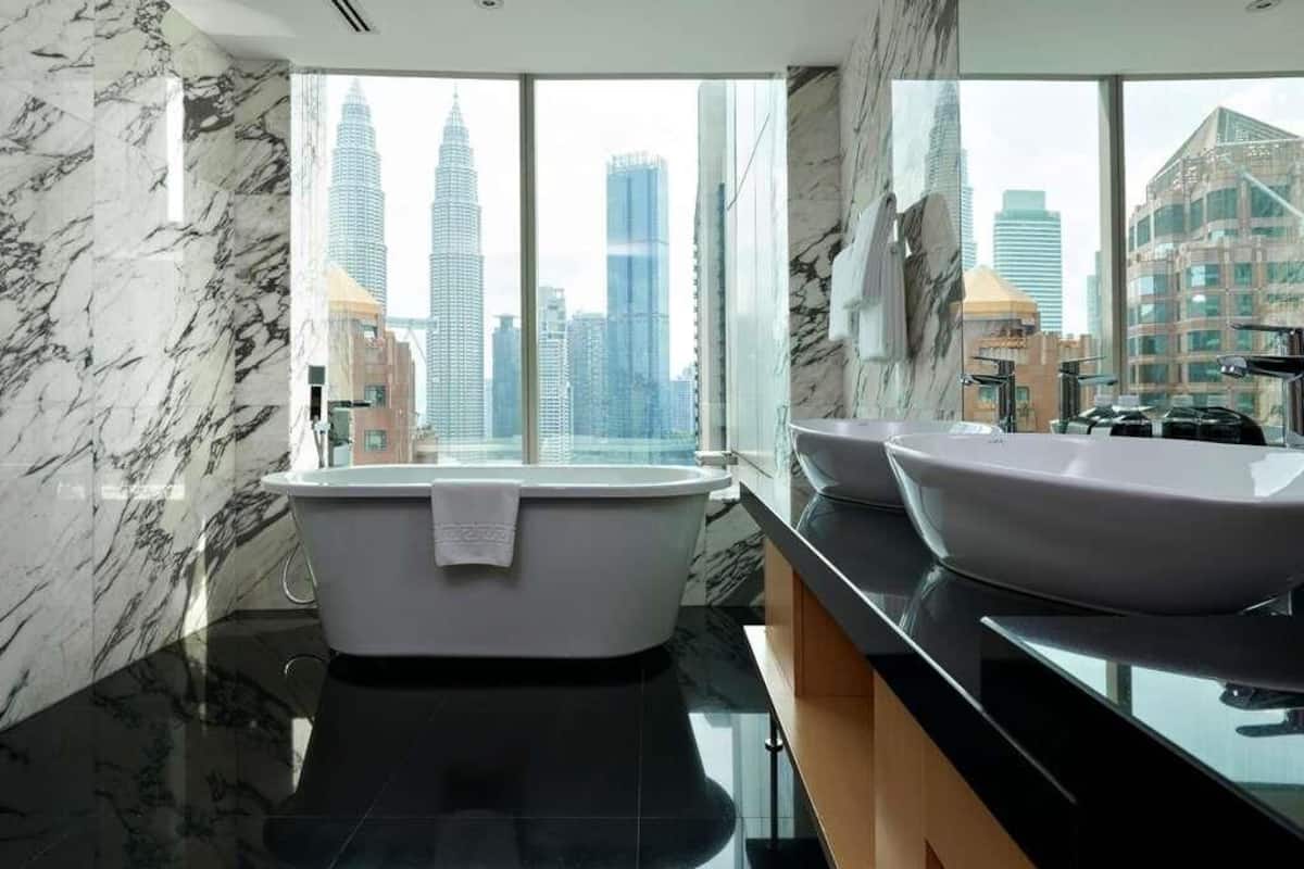 A modern bathroom with a bathtub, two sinks, and a large window offering a city view.