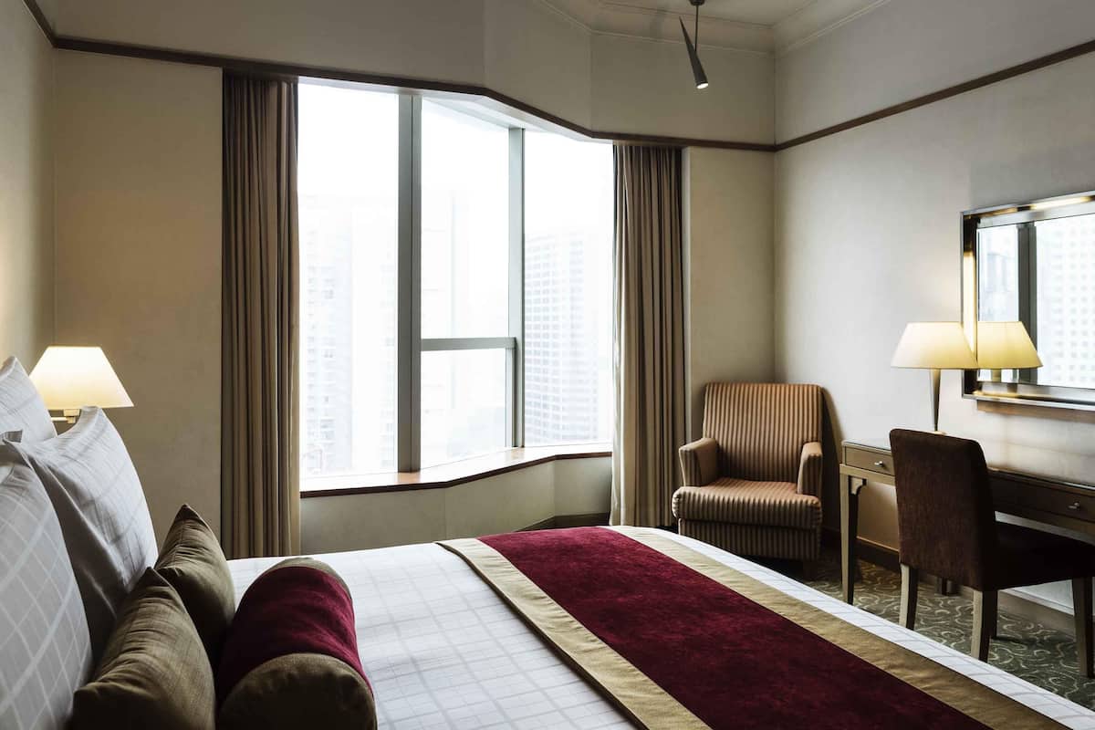 A hotel room with a large bed, a desk, a chair, and a window with curtains.