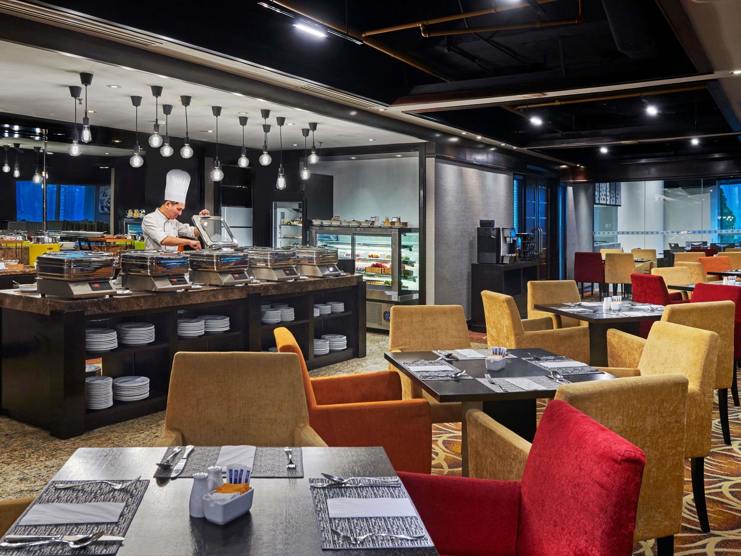 A modern restaurant with a chef preparing food, buffet stations, and a variety of seating options.