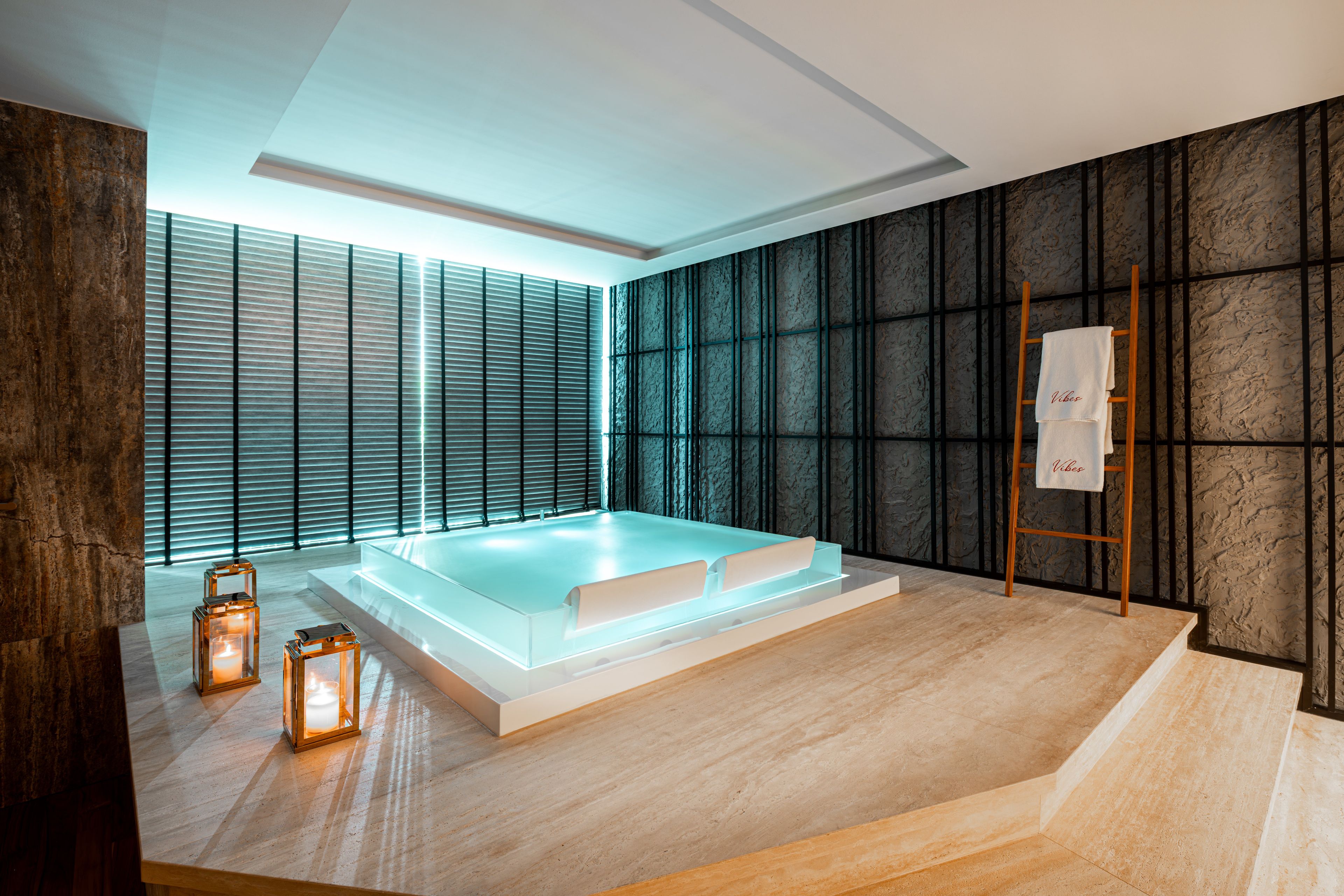 A modern spa room with a large bathtub, wooden floor, and a view through the window blinds.