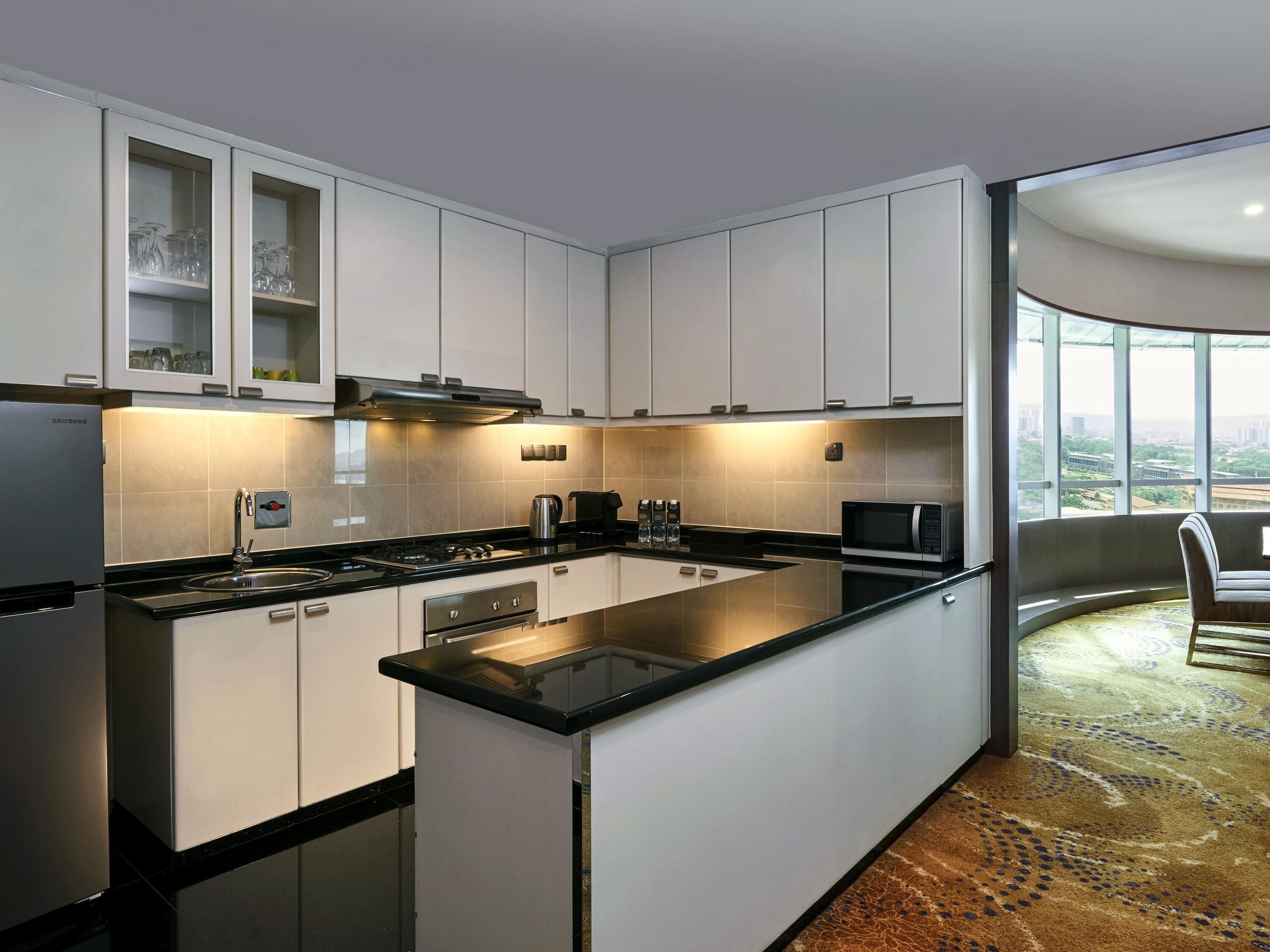 A modern kitchen with white cabinets, a black countertop, and a large window offering a city view.