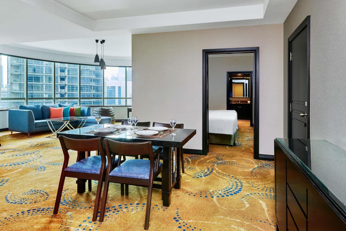 A hotel room with a dining area, a sofa, and a view of the cityscape.