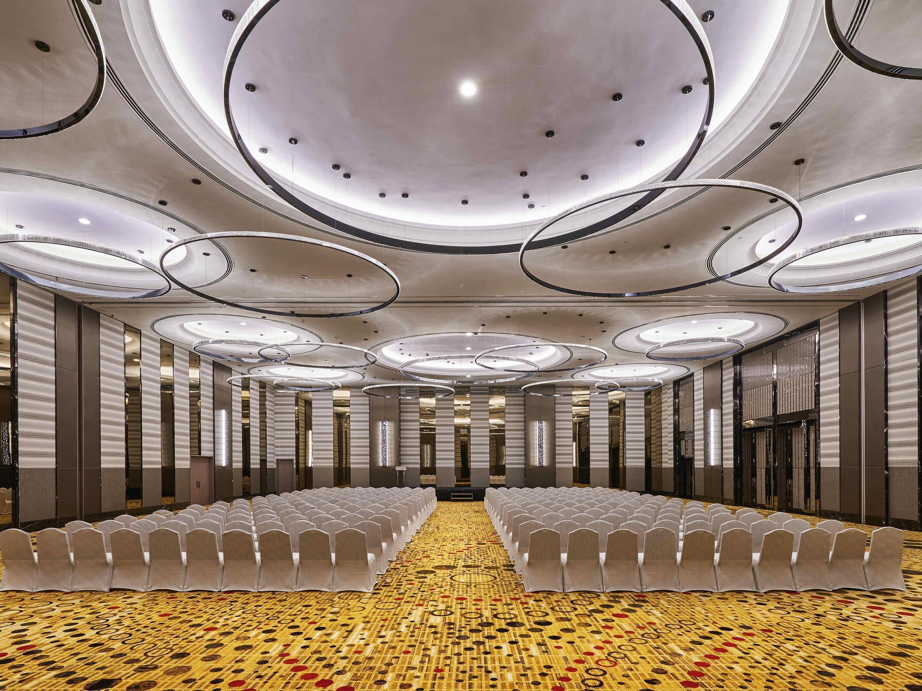 A spacious hall with rows of chairs, a patterned carpet, and a modern ceiling design.