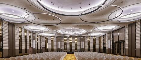 A spacious hall with rows of chairs, a patterned carpet, and a modern ceiling design.