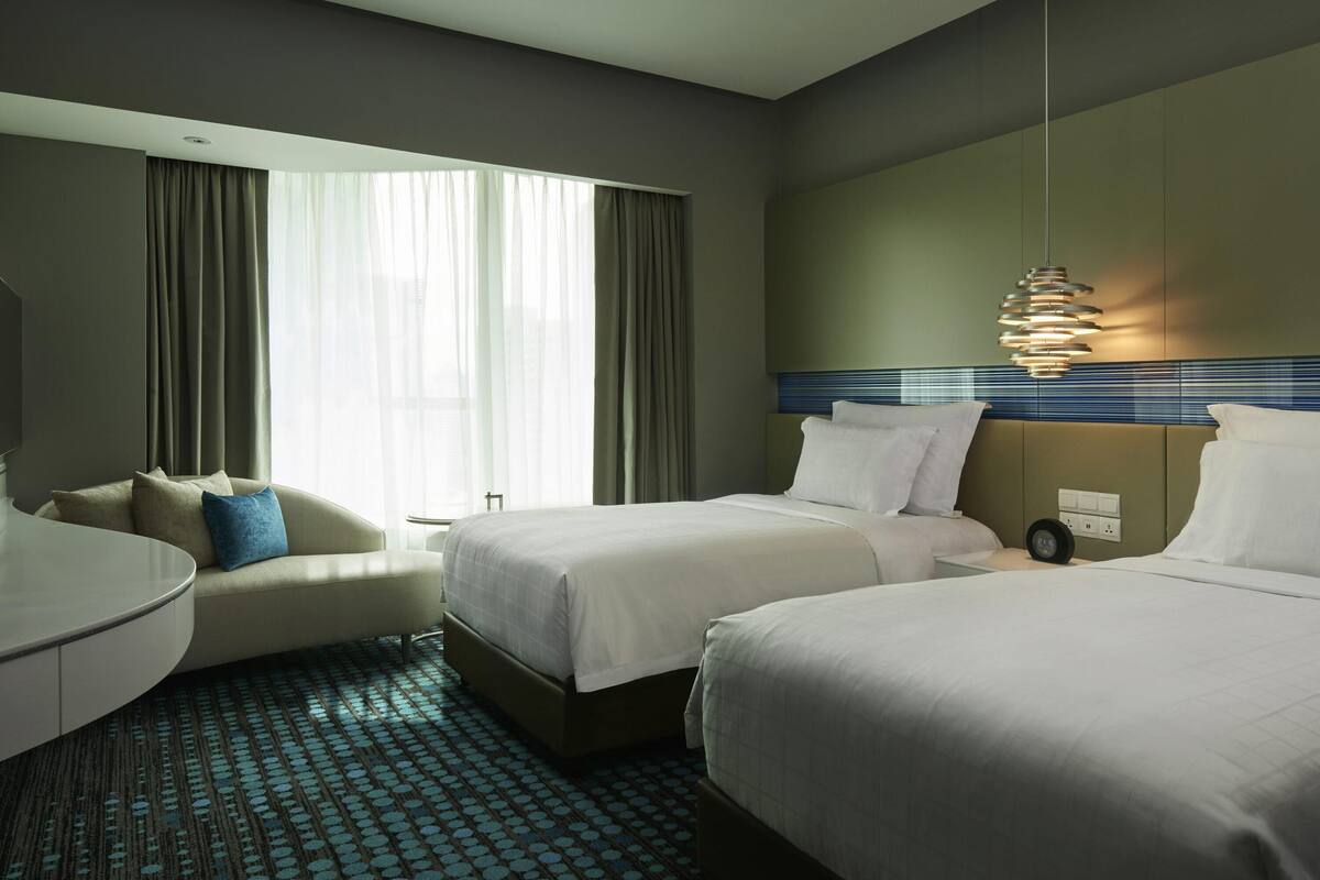 A hotel room with two beds, a sofa, a desk, and a large window with curtains.