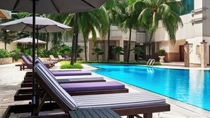 A poolside area with lounge chairs and umbrellas, a clear blue pool, palm trees, and a modern building in the background. - Pullman Kuala Lumpur City Centre Hotel & Residences (Kuala Lumpur)