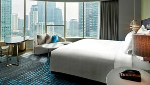 A hotel room with a large bed, a small round table, a sofa, and a view of tall buildings. - Pullman Kuala Lumpur City Centre Hotel & Residences (Kuala Lumpur)