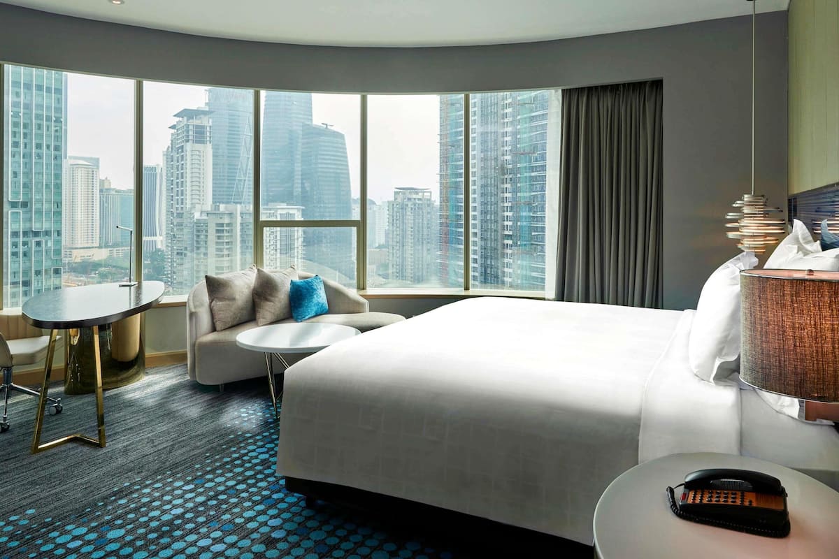 A hotel room with a large bed, a small round table, a sofa, and a view of tall buildings.