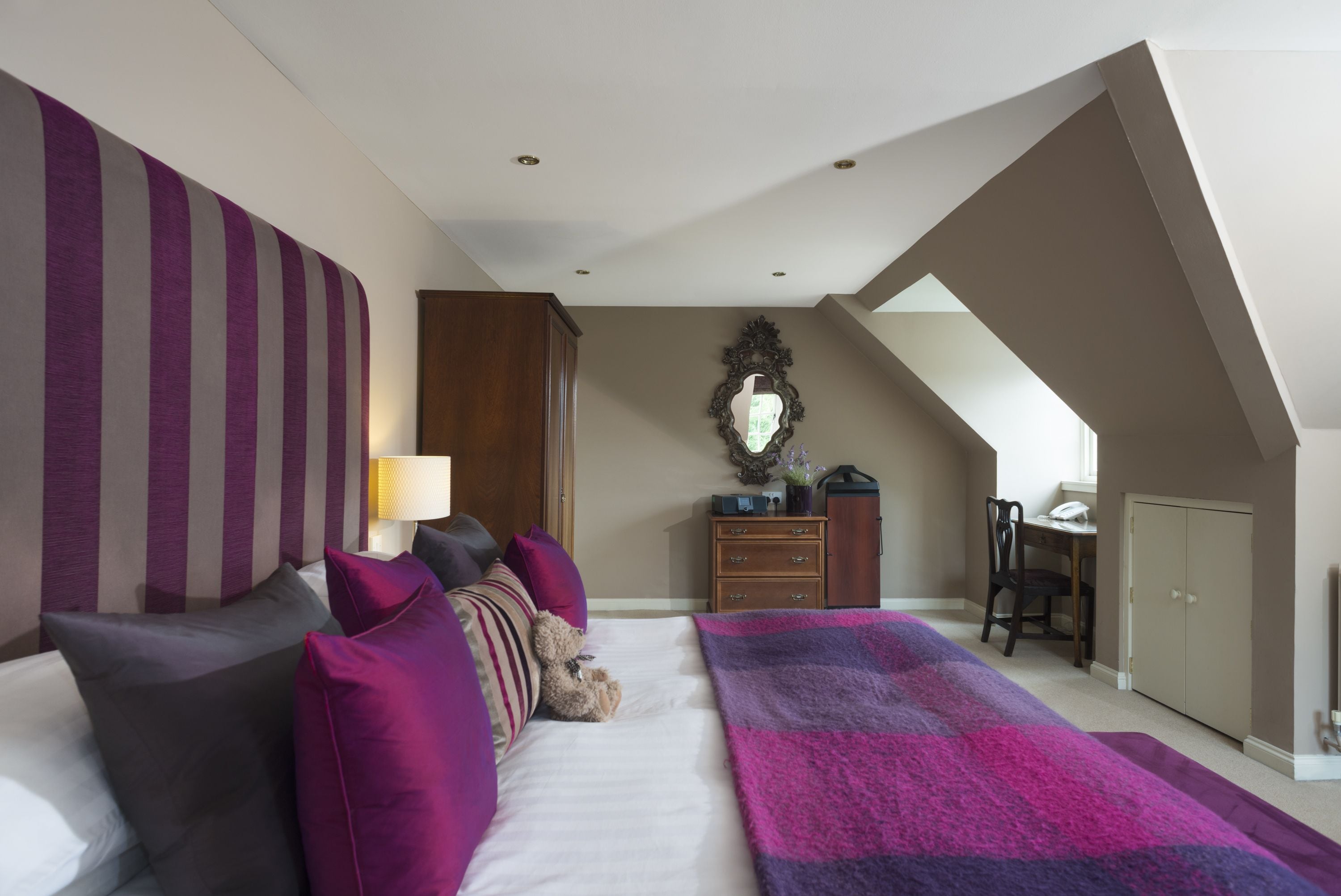 A bedroom with a bed, pillows, a blanket, a dresser, a mirror, and a desk with a chair.