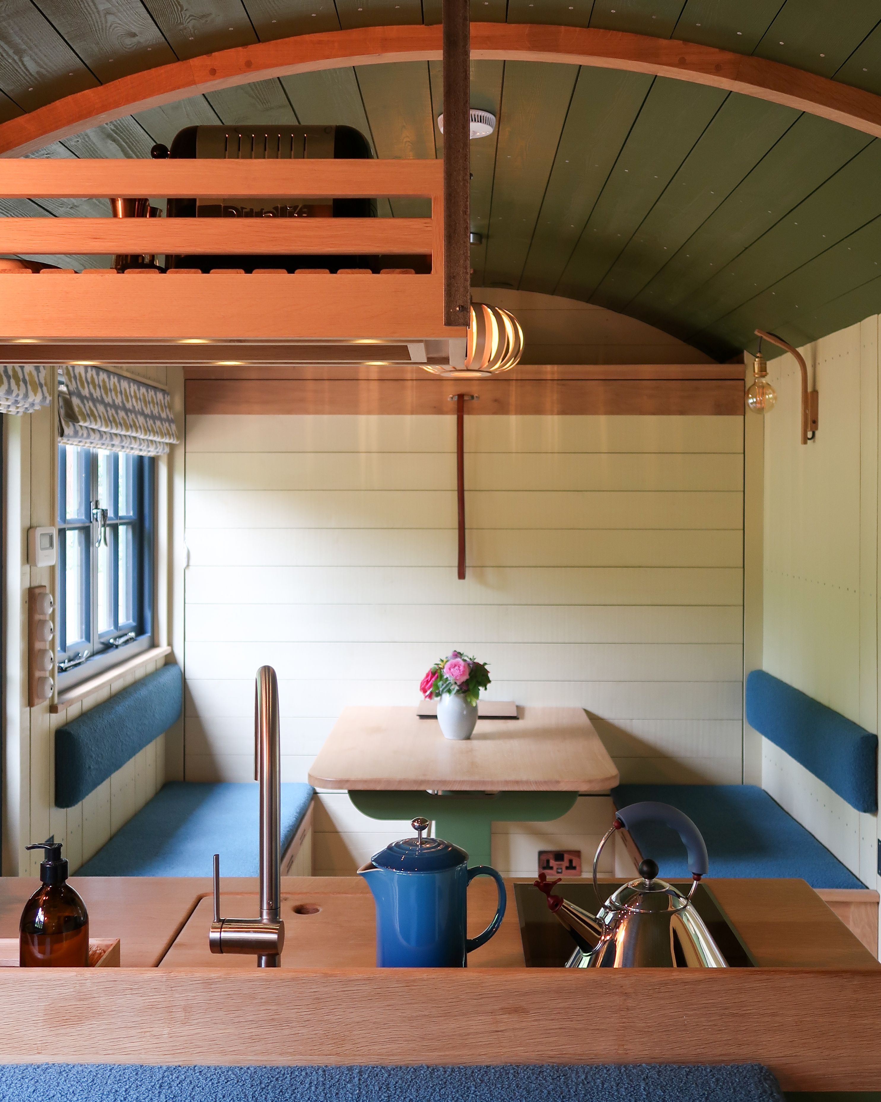 A compact, well-lit cabin with a bunk bed, a small table with a vase of flowers, and a kettle.