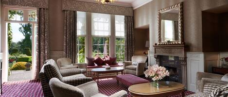 A spacious living room with a fireplace, comfortable seating, and large windows offering a view of the garden.
