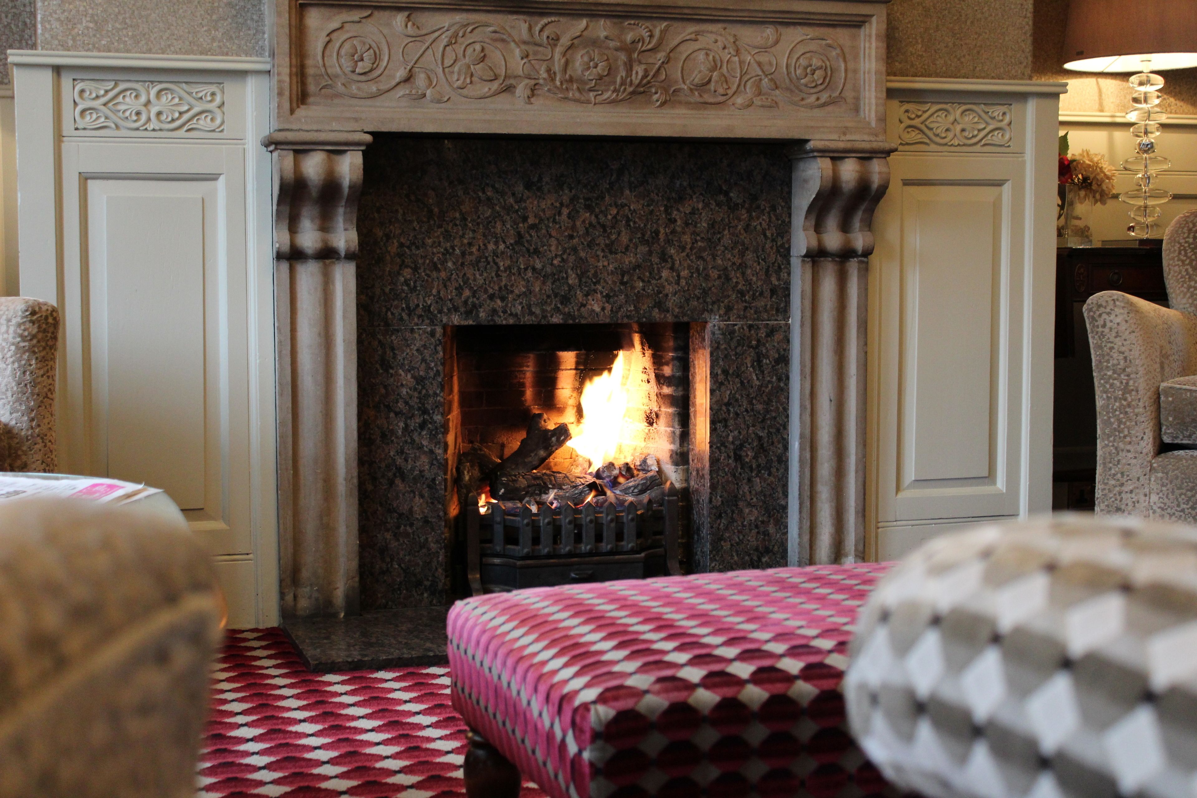 A fireplace with a fire, a checkered bedspread, and a patterned armchair.