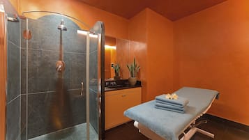 A modern bathroom with a glass shower enclosure, a massage table, and a sink area.