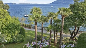 Un jardin aménagé avec des palmiers et des hortensias, un plan d’eau et un bateau au loin.