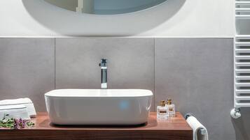 Un bagno moderno con un lavandino ovale bianco, uno specchio rotondo e un piano d'appoggio in legno.