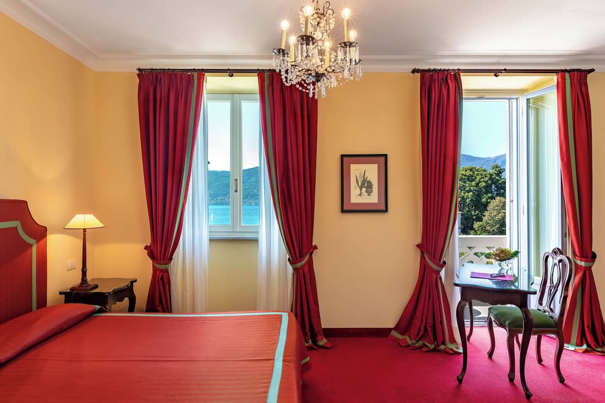 Hotelkamer met een bed, bureau, stoel, een kroonluchter en een raam met gordijnen.