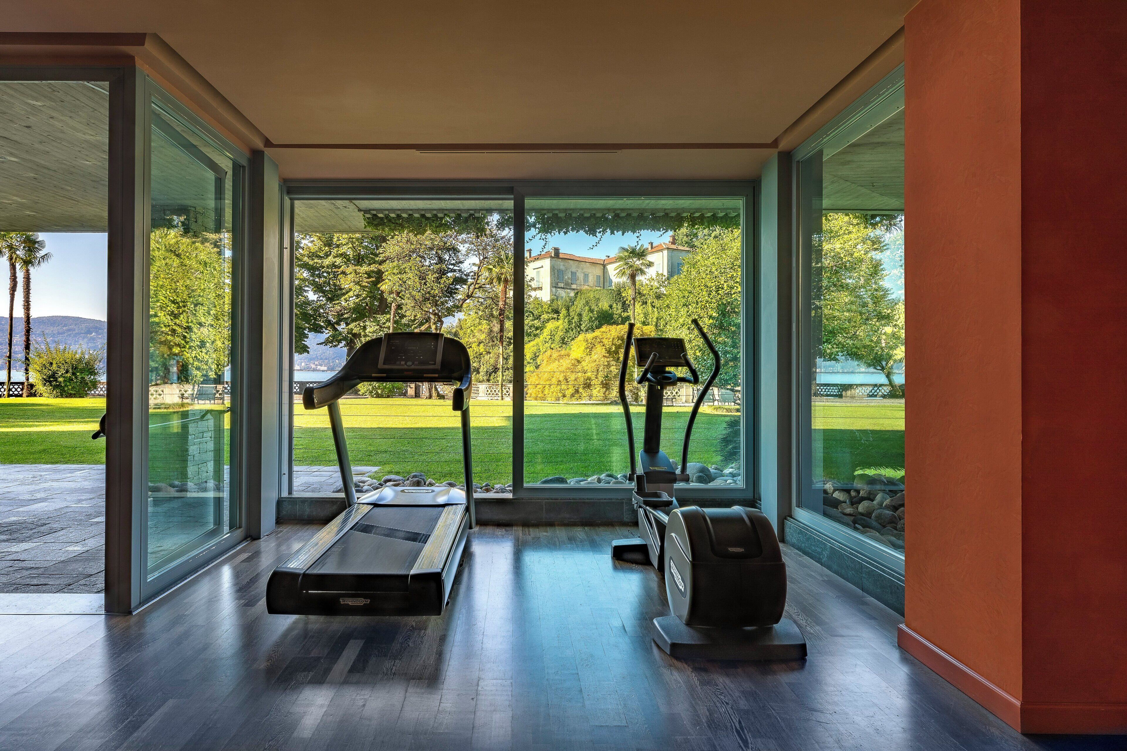 Ein moderner Fitnessraum mit Laufband und Ellipsentrainer, großen Glasüren und Blick auf eine grüne Landschaft.