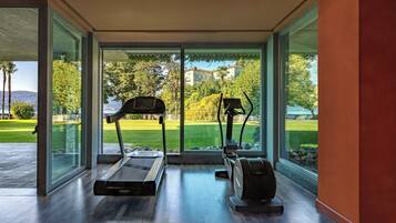 Ein moderner Fitnessraum mit Laufband und Ellipsentrainer, großen Glasüren und Blick auf eine grüne Landschaft.