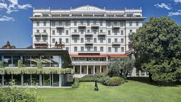 Un hotel grande de varios pisos con un estilo arquitectónico clásico, con balcones y un jardín bien cuidado.