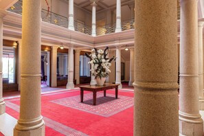 A grand lobby with high ceilings, large columns, a red carpet, and a central floral arrangement.