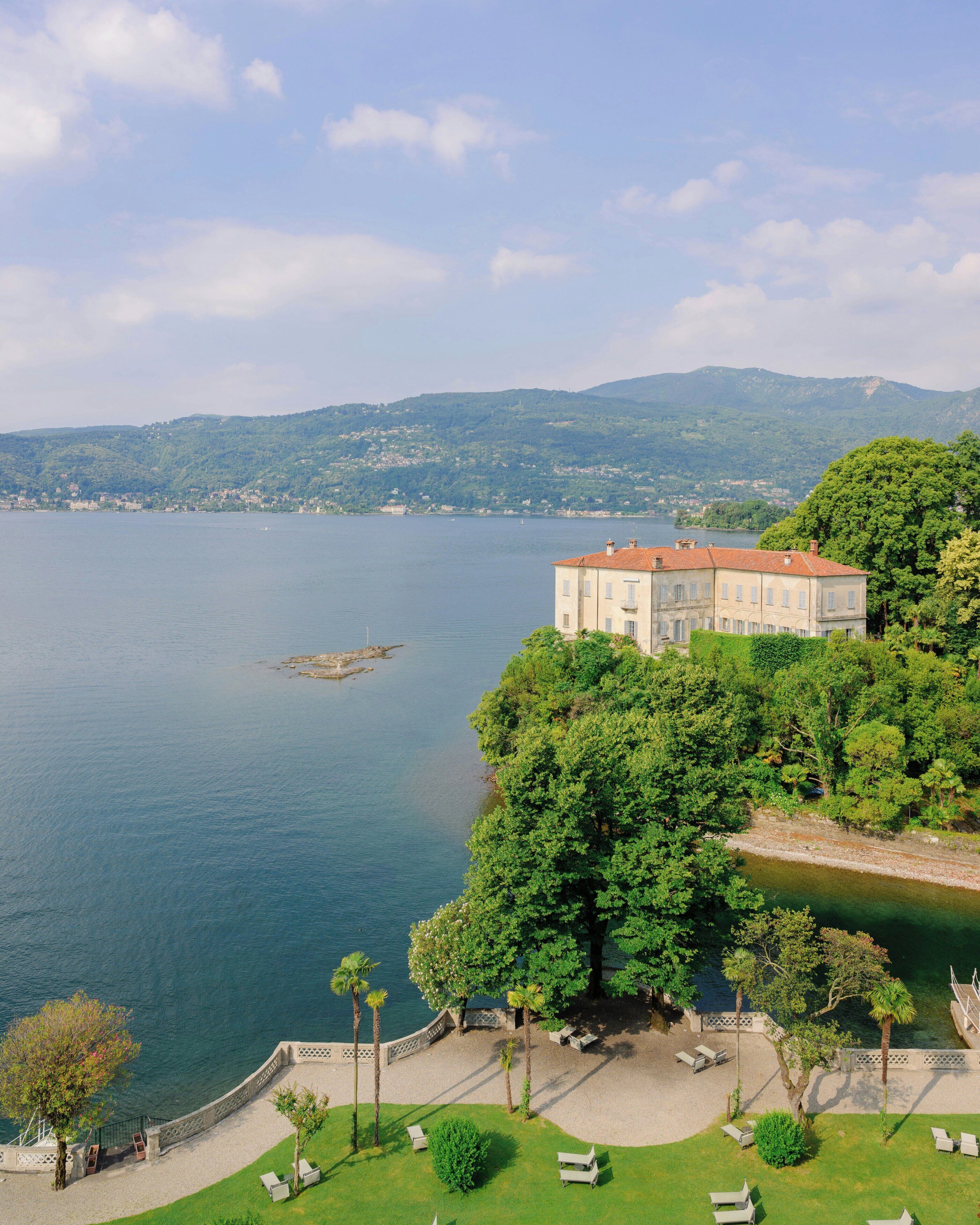 A large building with a red roof, surrounded by lush greenery and overlooking a calm body of water.