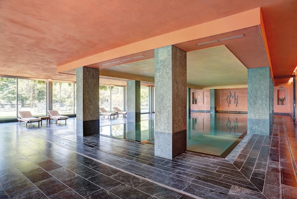 A spacious indoor area with a pool, lounge chairs, and large windows.