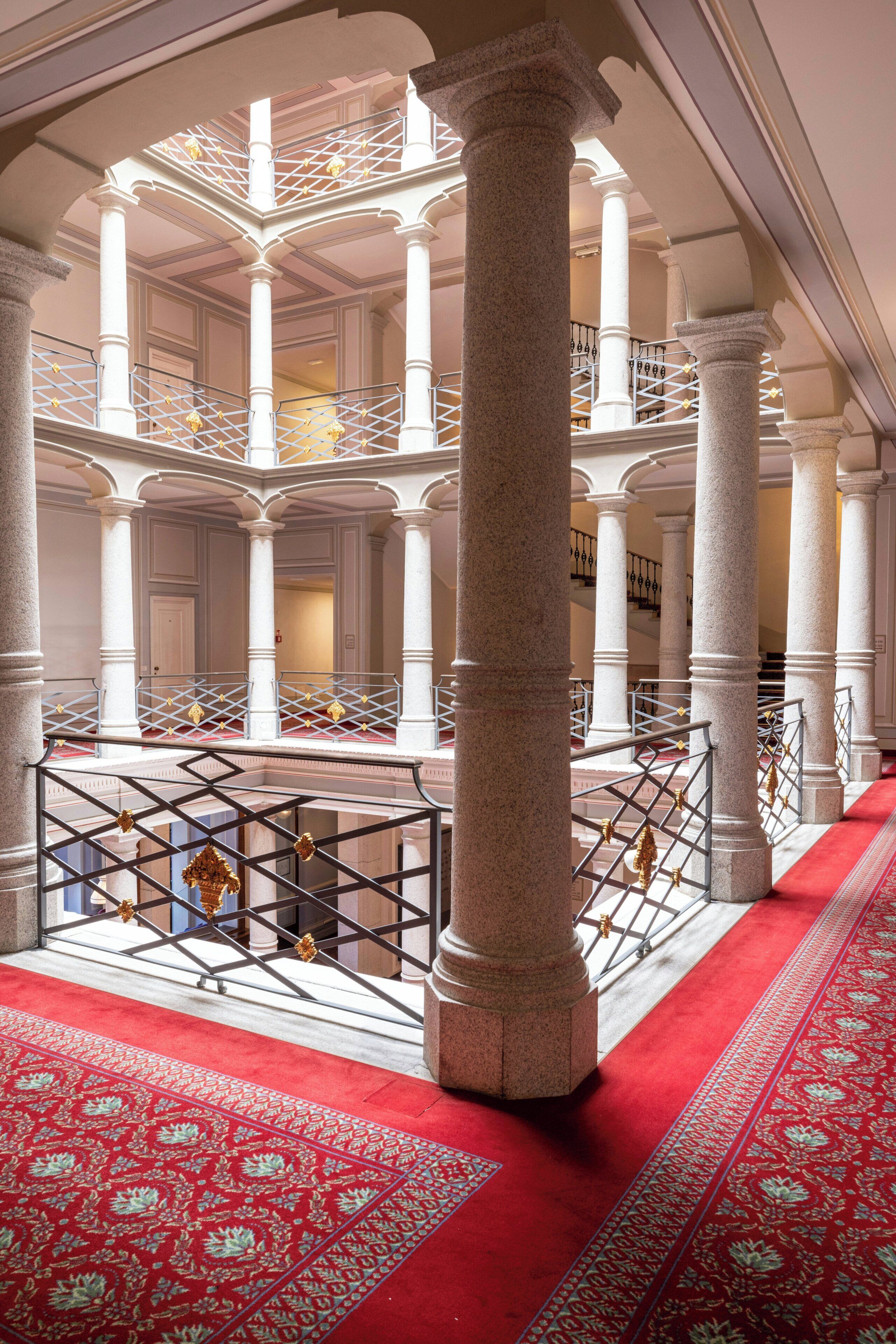 Un intérieur somptueux, avec plusieurs niveaux, des colonnes blanches et une zone recouverte d’un tapis rouge.