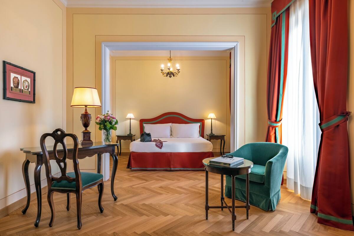Een hotelkamer met een bed, een bureau, een stoel, een lamp en een kroonluchter.